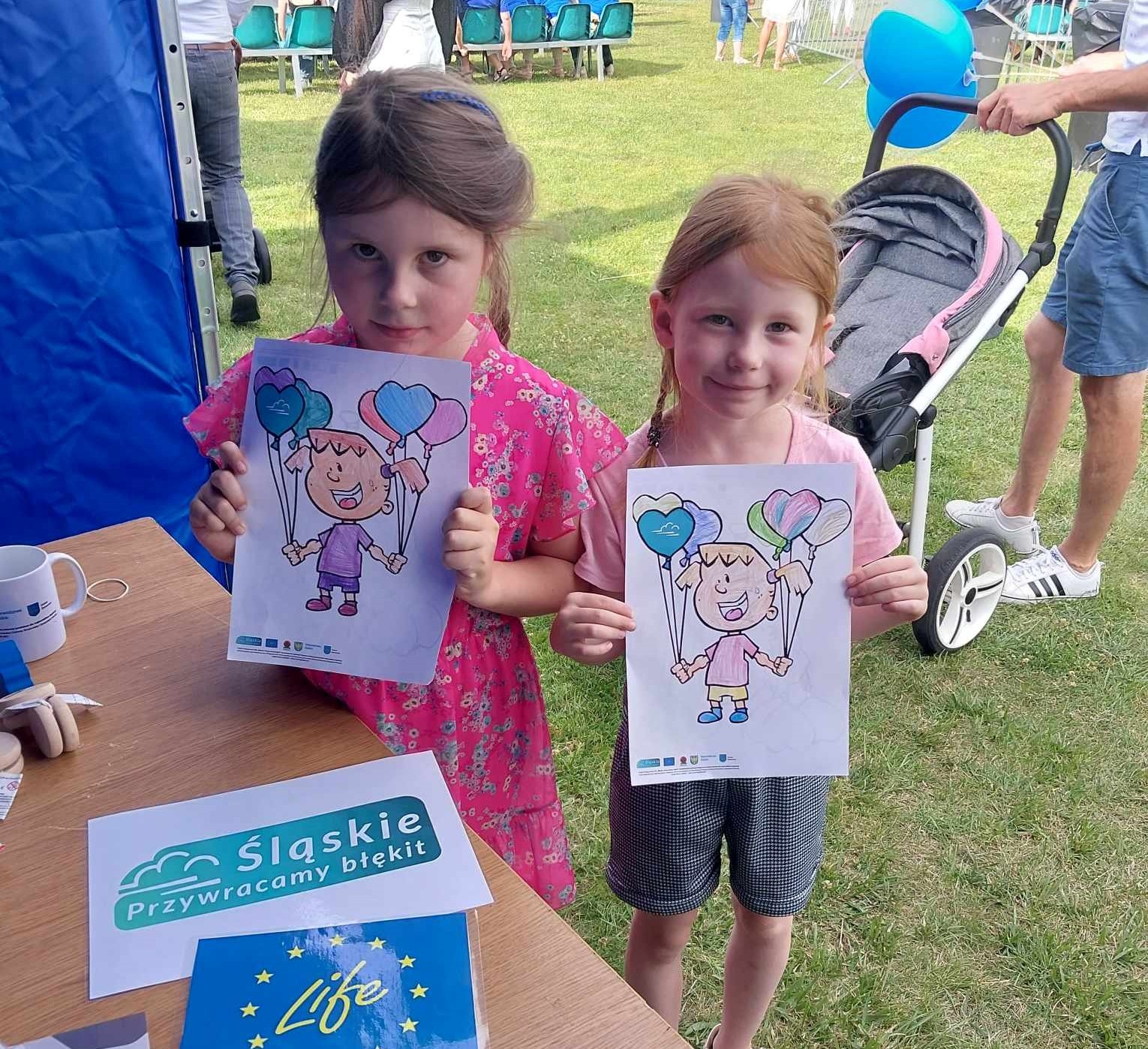 Two girls holding eco-themed coloring books at the picnic.
