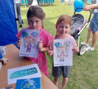 Two girls holding eco-themed coloring books at the picnic.