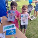 Two girls holding eco-themed coloring books at the picnic.