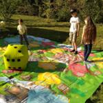 A group of children is playing a large board game laid out on the grass.