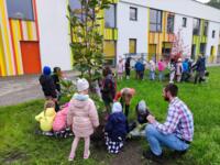 A group of preschoolers with the eco-manager Cezary Olchawa planting two trees on the lawn.