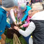A group of preschoolers with the eco-manager Cezary Olchawa planting two trees on the lawn.