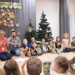 A group of preschoolers sitting with the eco-manager in a circle on the floor inside the preschool classroom. In the background, a decoration mimicking a forest.