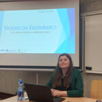 The subregional eco-manager sitting at a table with the presentation displayed in the background.