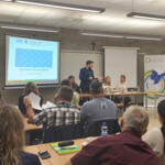 A group of eco-managers sitting in benches and listening to the coordinator's presentation.