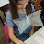 A girl blowing into a plastic bag through a straw.
