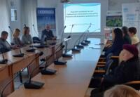 A group of adult participants at the meeting watching presentations displayed on the screen.