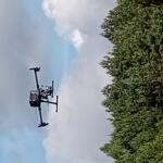 Dron w locie ponad drzewami na tle nieba.