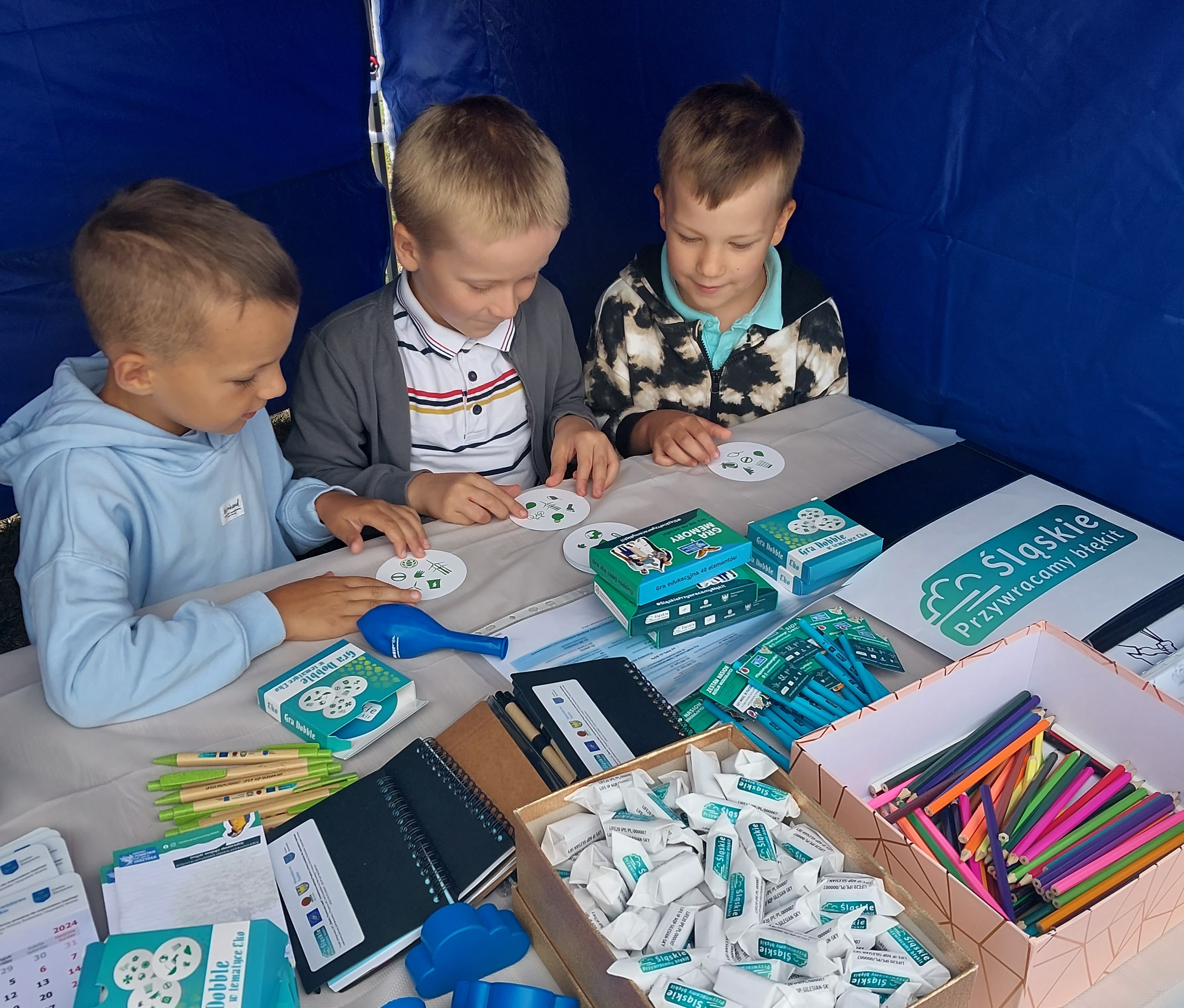 Dzieci oglądające materiały edukacyjne na stoisku ekodoradcy.